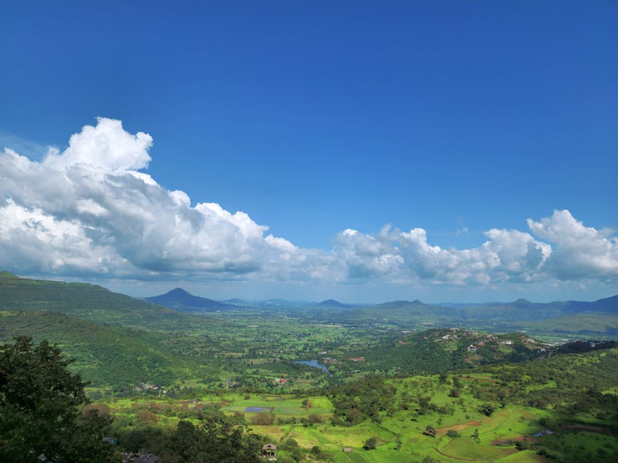 Stunning aerial view of lush green countryside under a clear blue sky with fluffy clouds, showcasing nature's beauty.